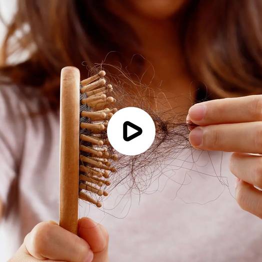 Eine Person hält eine hölzerne Haarbürste mit Haarsträhnen, die sich in den Borsten verfangen haben, während sie mit der anderen Hand lose Haare aus der Bürste zieht.